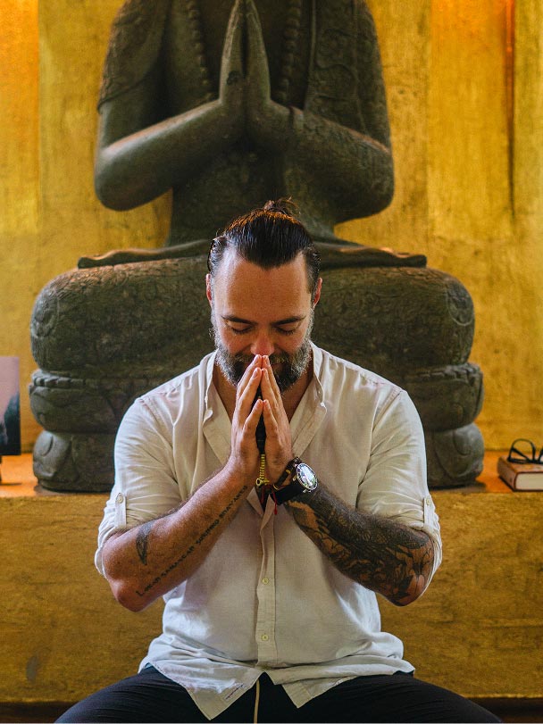 Pema, guía de meditación de Alma Loto, sentado en postura contemplativa frente a una figura de Buda